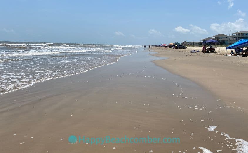 Looking down the beach, lots of flat sand and shallow water.